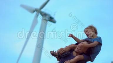 父子俩玩得很开心，站在海边山顶的风力发电机下。 清洁能源概念